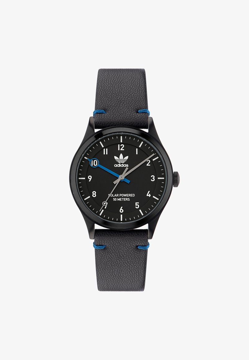 Melnā saules enerģijas rokas pulksteņa ar apaļu seju, baltiem stundas marķieriem, zilas akcenta otrajā rokā un teksturētu pelēku ādas siksniņu.