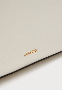 Sac à main en cuir synthétique blanc texturé avec logo "ALDO" doré. Présente une bordure noire le long du bord. Surface lisse sans motifs.