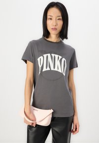 Camiseta gris de manga corta con el logo en blanco "PINKO" en negrita, combinada con un bolso de cuero rosa claro y pantalones de cuero sintético negros.