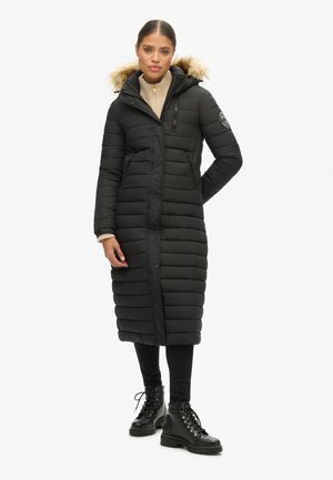 Manteau rembourré noir avec une capuche doublée en fausse fourrure, poches zippées et un design longueur genoux. Matelassage texturé horizontal sur toute la surface.