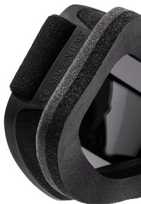 Juoda aksesuaras, pagamintas iš patvarių medžiagų, su tekstūruota paviršiaus danga. Prieduose yra velcro dirželiai ir įspaustas užrašas "MADE IN ITALY." Elegantiškas, lenktas dizainas.