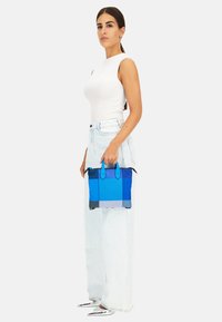 Borsa strutturata blu con due manici superiori, che presenta una miscela di texture e sfumature dal blu chiaro al blu scuro. Indossata da una persona in denim chiaro.