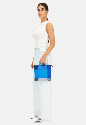 Borsa strutturata blu con due manici superiori, che presenta una miscela di texture e sfumature dal blu chiaro al blu scuro. Indossata da una persona in denim chiaro.