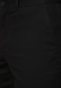 Czarne bawełniane spodnie o teksturowanym wykończeniu i subtelnym detalem z logo, z standardowymi kieszeniami i dopasowanym krojem.