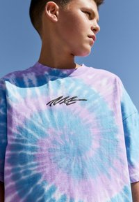 Tricou tie-dye în bleu deschis și lavandă, având un logo negru pe piept. Material din bumbac cu o croială lejeră și guler rotund.