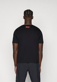 Zwarte t-shirt van katoen, met een ronde halslijn en een klein rood logo op de bovenrug. Korte mouwen en een relaxte pasvorm.