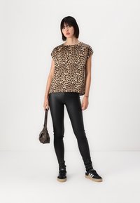 Bluza s uzorkom leoparda u svijetlosmeđoj boji s crnim točkicama, kombinirana s crnim tajicama od umjetne kože i crnim tenisicama s gumiranim potplatima. Smeđa torba.