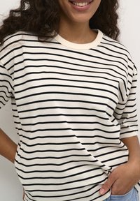 Camiseta a rayas de tejido ligero, con rayas horizontales en negro y crema, cuello redondo y mangas cortas.