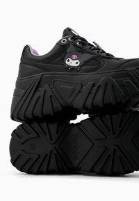 Black chunky sneakers with a textured rubber sole, featuring a cartoon character logo on the side and purple accents on the tongue.