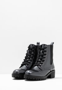 Botas negras de tobillo con un acabado texturizado, con cordones en la parte delantera, paneles laterales elásticos y tacones anchos.