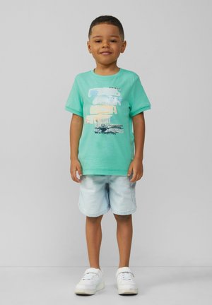 Miętowy bawełniany t-shirt z graficznym nadrukiem, w połączeniu z jasnymi dżinsowymi szortami. Białe trampki dopełniają całość stroju.