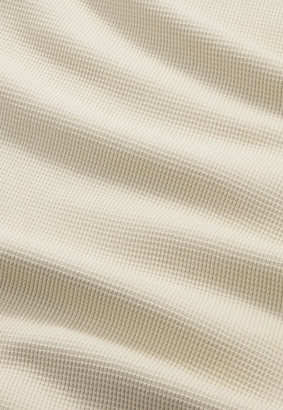 Tissu beige avec une petite texture en nid d'abeille, présentant de doux plis et des ombres subtiles à la surface.