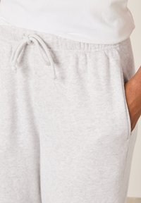 Gaiši pelēkas sporta bikses no mīksta auduma ar auklas jostu viduklī un sānu kabatām ar gludu, teksturētu virsmu.