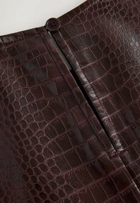 Indumento in pelle sintetica bordeaux con un motivo testurizzato a coccodrillo, dotato di una cucitura visibile, chiusura con zip e un accento di bottone scuro.