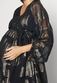 Svart klänning med transparenta ärmar och gyllene metalliska blommönster, med V-ringning, insvängd midja och en flödande kjoldesign.