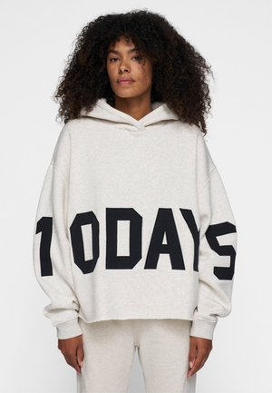 Sudadera corta en gris claro hecha de un material suave, con letras negras en bloque que dicen "10 DÍAS" en el frente. Incluye una capucha amplia y un corte holgado.