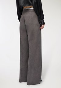 Spodnie o szerokich nogawkach w gładkiej, teksturowanej szarej tkaninie. Posiadają wysoki stan i subtelny połysk, z czystymi linii i bez widocznych elementów sprzętowych.