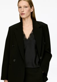 Black blazer with double-breasted buttons and structured shoulders, worn over a black satin camisole featuring a lace trim.