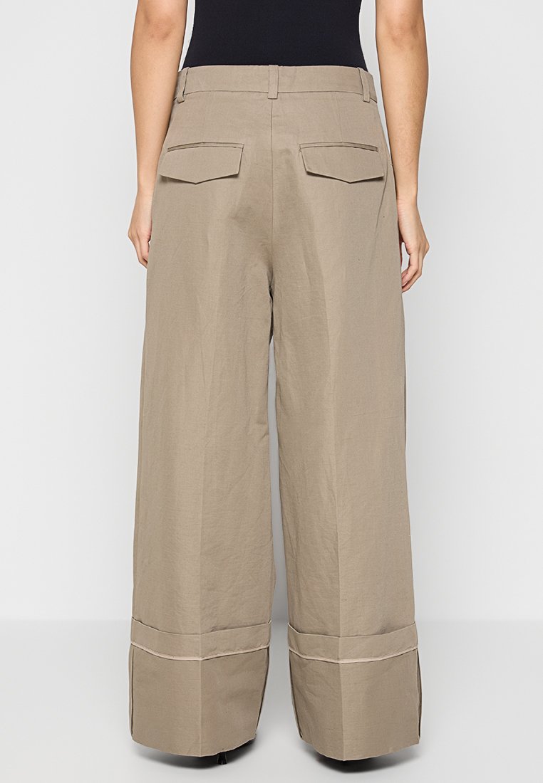 Beige wijde broek met hoge taille, twee achterzakken en detailafwerking aan de zoom. Gemaakt van lichte stof met een gladde textuur.
