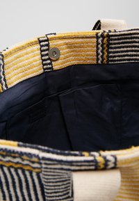 Interno di una borsa tessuta multicolore con rivestimento in tessuto blu navy, caratterizzato da strisce orizzontali gialle e blu navy, e una chiusura con bottone a pressione argentato.
