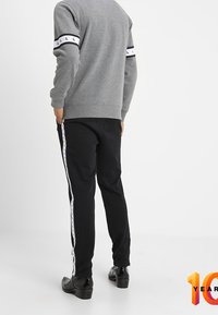 Felpa grigia con polsini a righe bianche e nere, abbinata a pantaloni neri con logo bianco lungo i lati. Tessuto liscio, design aderente.