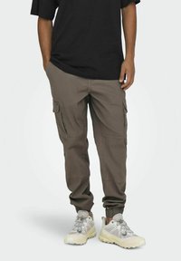 Pantalones cargo en verde oliva, con múltiples bolsillos laterales, puños elásticos y un corte relajado, combinados con zapatillas gris claro.