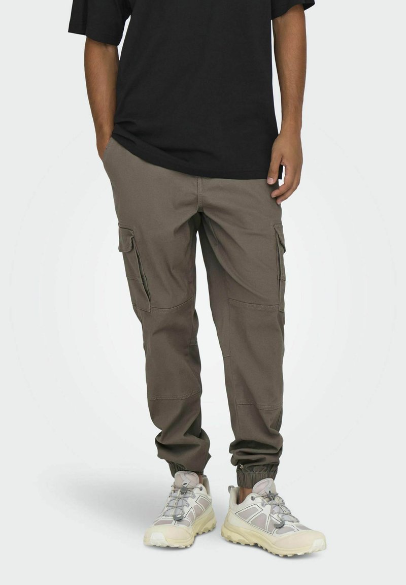 Pantalones cargo en verde oliva, con múltiples bolsillos laterales, puños elásticos y un corte relajado, combinados con zapatillas gris claro.