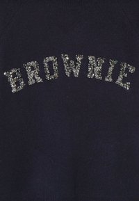 Pull marin avec des lettres en sequins épelant "BROWNIE" dans un design incurvé. Le tissu semble doux et texturé, avec un style décontracté.
