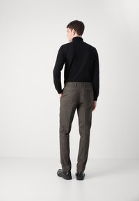Crni džemper s rol kragnom, smeđe hounds-tooth hlače i crne cipele. Outfit ima uski kroj i detalje od teksturirane tkanine.