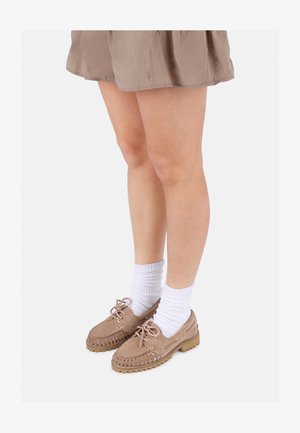 Hellbraune Wildlederschuhe mit geflochtenem Muster, Schnürung vorne und Gummisohle, kombiniert mit weißen gerippten Socken und einem beigen Rock.