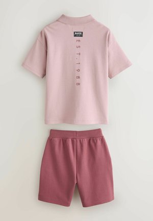 Hele roosa lühikeste varrukatega polosärk, millel on seljal silt; kombineeritud bordoopunaste lühikeste pükstega, millel on elastne vöökoht. Lihtne disain.