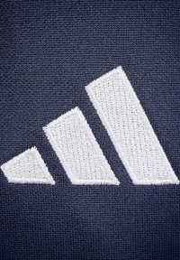 Marineblauw textiel met een opvallend wit geborduurd logo met drie diagonale strepen, ontworpen met een gestructureerde afwerking.