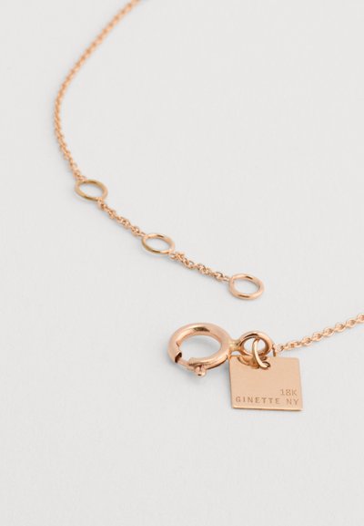 18K rožinio aukso grandinėlė pasižymi apvalių žiedų dizainu, su krabų tipo klaspele ir stačiakampiu tagu, kuriame įrašyta "GINETTE NY."