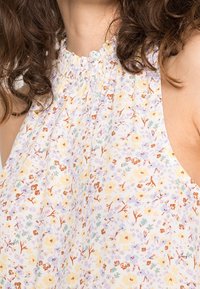 Blomstret ærmeløs top i let stof med rynket halsudskæring. Den har en pastel farvepalet med små, flerfarvede blomsterprint.