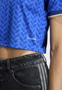 Blue cropped shirt with a leaf pattern, featuring "CLIMA COOL" logo. Paired with black pants showcasing textured fabric and side stripes.