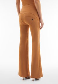 Pantaloni marroni a campana con una texture liscia, dotati di tasche posteriori e un piccolo accento con logo. L'orlo è leggermente svasato nella parte inferiore.