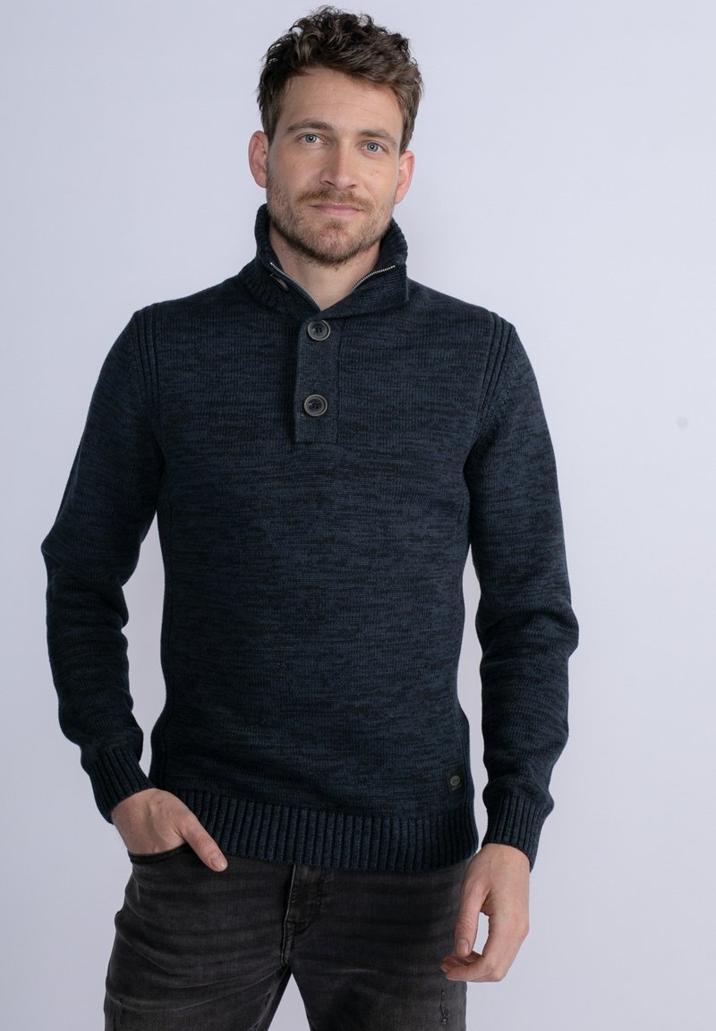 Maglione lavorato a maglia blu scuro con colletto alto, due grandi bottoni, polsini e orlo a coste, che mostra un motivo testurizzato in tutta la sua superficie.