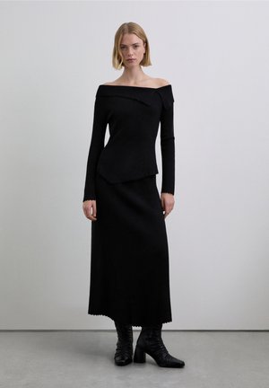 Vestido negro sin hombros con mangas largas, cuerpo ajustado, bajo asimétrico, tejido texturizado, combinado con botas negras hasta la rodilla.