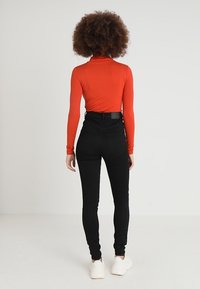 Top rojo de manga larga combinado con jeans ajustados negros de cintura alta. El conjunto se completa con zapatillas blancas y presenta un diseño sencillo.