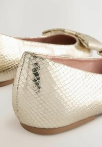Kultaiset metalliset ballerinat, joissa on teksturoitu käärmeennahkakuosi, pyöristetty kärki ja suuri nauha etuosassa. Tasapohja näkyvissä.