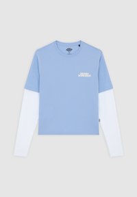 Hellblaues Kurzarmhemd, darüber ein weißes Langarmhemd getragen, mit einem dezenten Logodesign auf der Brust. Baumwollstruktur.