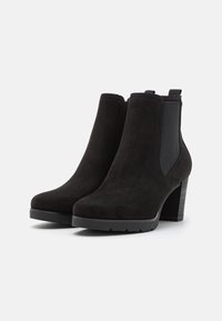 Bottines en daim noir avec un bout arrondi, des empiècements élastiques sur les côtés et un talon épais pour la stabilité. Surface texturée et design minimaliste.