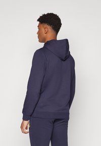 Marineblå bomulds sweatshirt med snøre i hætte, ribbede manchetter og kant, blød tekstur og en afslappet pasform, vist fra ryggen.
