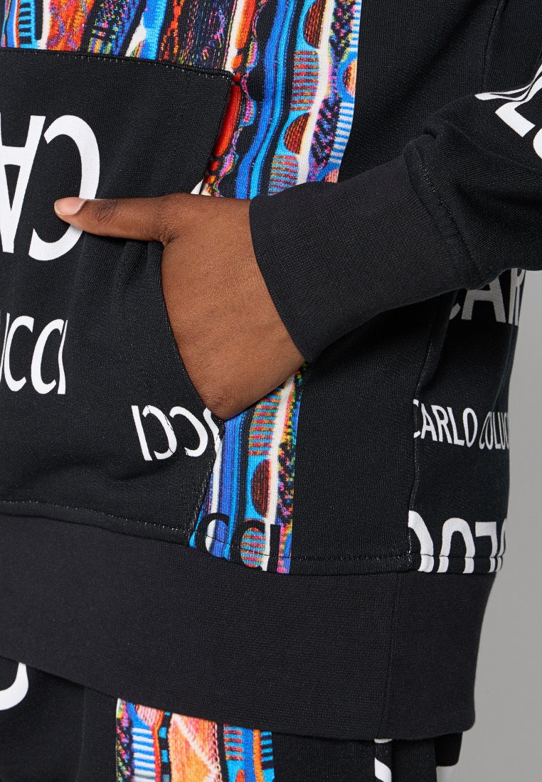 Sudadera negra con acentos de patrones coloridos, letras blancas en contraste y un bolsillo frontal. Tejido texturizado con un ajuste relajado.