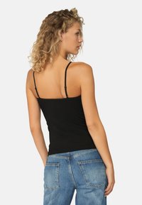 Zwarte getailleerde tanktop met dunne bandjes, gladde stof, achterkant met lichte ruching, gecombineerd met lichtblauwe distressed jeans.