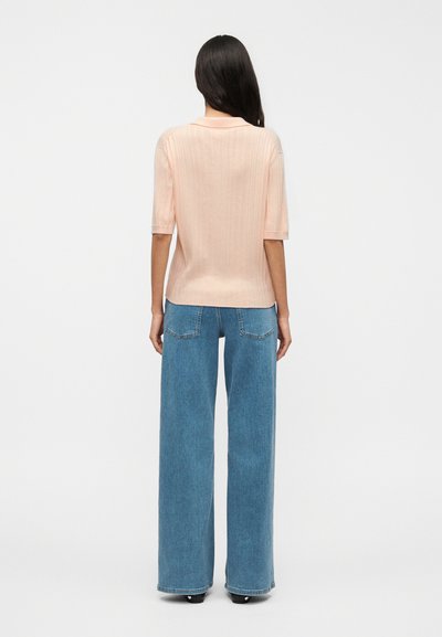 Ροδακινί πλεκτό τοπ με κοντά μανίκια, συνδυασμένο με τζιν παντελόνι μπλε χρώματος, ψηλόμεσο, με φαρδιά πόδια, πίσω τσέπες και άνετη εφαρμογή.