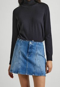 Jupe en denim mini de couleur bleu clair, avec un ourlet effiloché, une fermeture centrale par boutons et des coutures verticales ; associée à un pull col roulé noir.