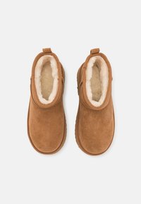 Botas de tobillo de ante marrón con un forro de color crema suave y un bucle trasero para facilitar el calzado. Suela de goma plana. Textura suave, punta redondeada.