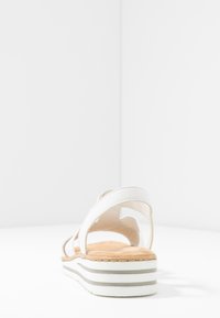 Sandale blanche avec plusieurs brides, semelle intérieure rembourrée et semelle stratifiée avec une base blanche et des accents gris. Texture en cuir lisse.