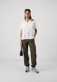 Cămașă albă cu mânecă scurtă, cu butoane, având două buzunare la piept, pantaloni cargo verzi măsliniu și adidași gri. Accesorizată cu o geantă mică neagră.